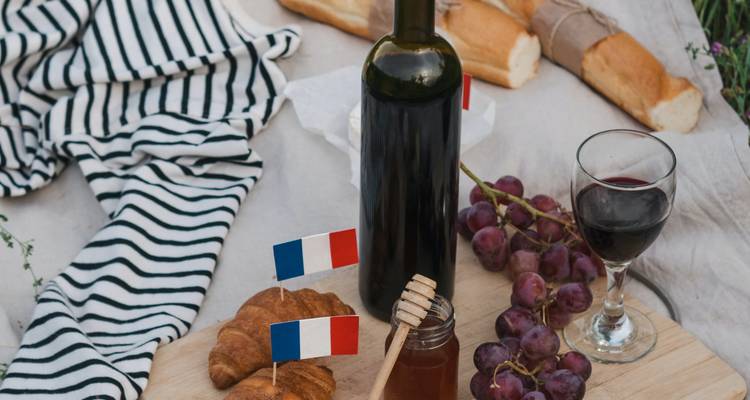 Picnic board with baguettes, croissants, wine and French flags on rustic cloth
