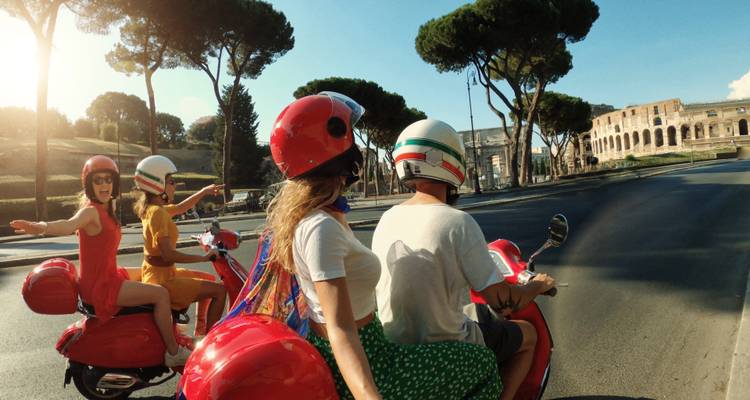 Jonge reizigers die op rode Vespas langs het Colosseum van Rome rijden op een zonnige dag, met uitgestrekte armen van opwinding.
