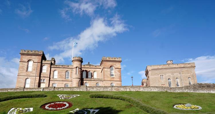 El Castillo de Inverness se encuentra en la cima de un terraplén cubierto de hierba con una bandera escocesa ondeando bajo un cielo azul despejado