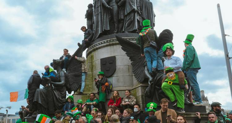 Une foule célébrant au sommet et autour d'un grand monument décoré de drapeaux irlandais et de costumes.