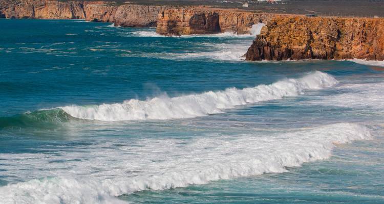 Mächtige Atlantikwellen, die gegen die raue orange Küstenlinie von Sagres prallen.