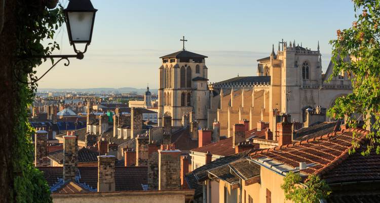 Vista de la azotea del barrio histórico de Lyon con torres de iglesia y chimeneas de terracota al amanecer.