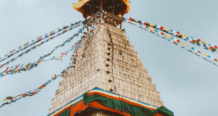 Une tour de stupa blanche drapée de drapeaux de prière multicolores s'élève vers un ciel bleu cristallin.