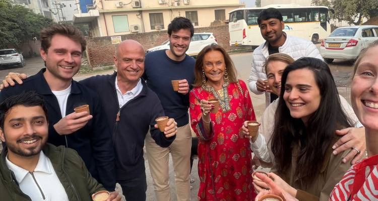 Fröhliche Gruppe von Touristen, die auf einer Straße in Delhi Chai aus Tongefäßen genießen, mit einem Reisebus im Hintergrund.