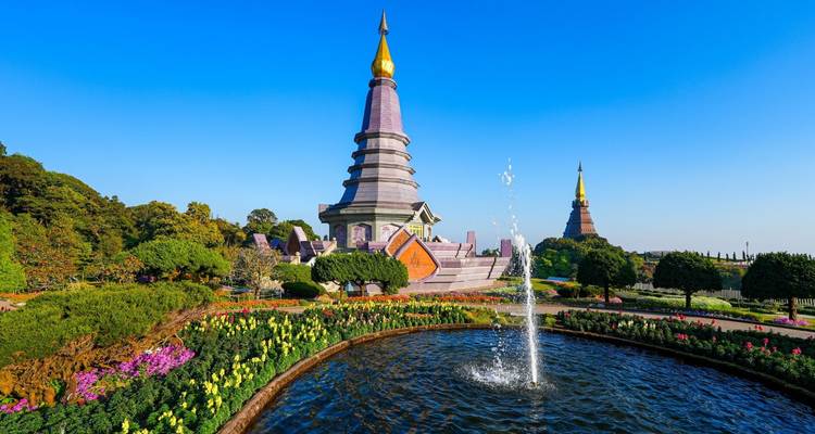 Les deux chedis du parc national de Doi Inthanon encadrés par des jardins soignés et une fontaine sous un ciel bleu.