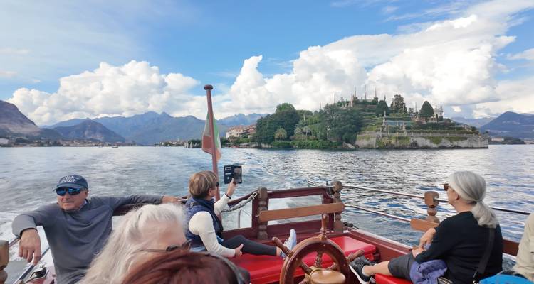 Les voyageurs se détendent à bord d'un bateau à moteur en bois naviguant sur un lac alpin pittoresque en direction d'un village insulaire.