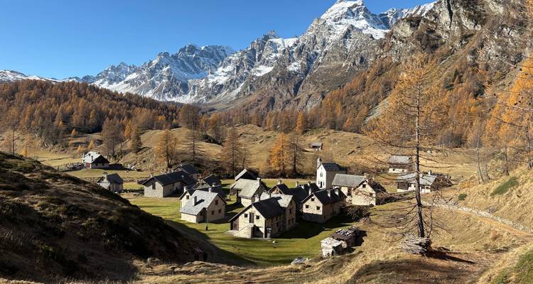 Petit hameau alpin isolé niché dans une vallée de mélèzes dorés sous des pics enneigés spectaculaires.