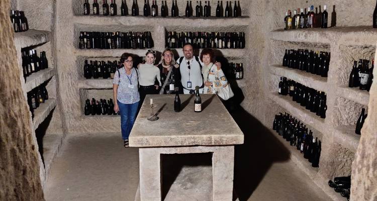 Un petit groupe pose à l'intérieur d'une cave à vin souterraine bordée de bouteilles poussiéreuses.