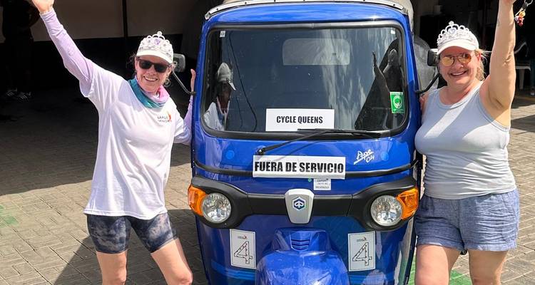 Twee blije vrouwen met diadems poseren met een felblauwe tuk-tuk met het opschrift 'Cycle Queens'.