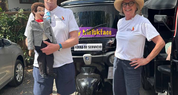 Reizend stel met een buikspreken pop staat naast een zwarte tuk-tuk genaamd 'TukTukface'.