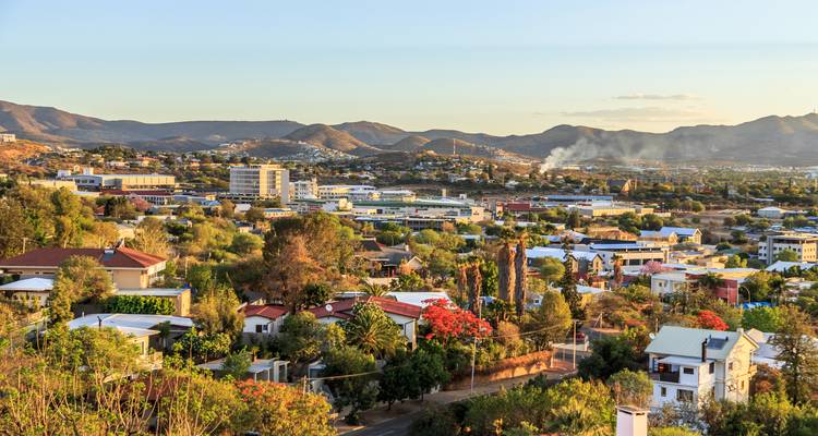 Suburbaan Windhoek-landschap met bloeiende bomen en rokerige heuvels tijdens het gouden uur.