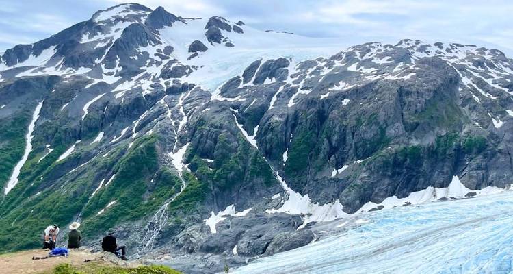 Des randonneurs se reposant sur une crête à côté d'un vaste glacier de l'Alaska avec des pics enneigés s'élevant derrière eux.