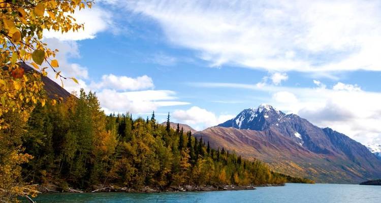 Lac turquoise serein bordé par une forêt automnale avec les montagnes enneigées de l'Alaska en arrière-plan.