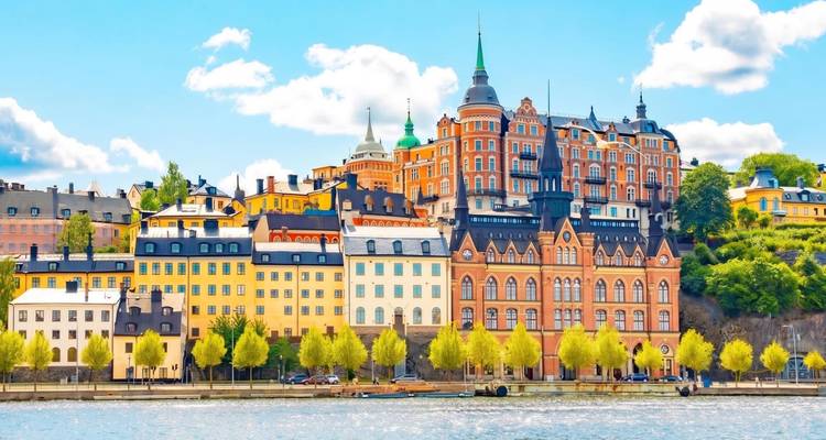 Edificios históricos de colores vibrantes del barrio Södermalm de Estocolmo reflejados en aguas tranquilas en un día soleado.
