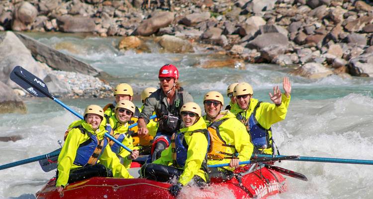 Équipe dynamique de rafting en eaux vives vêtue d'équipement jaune vif naviguant avec puissance à travers les rapides et saluant la caméra.