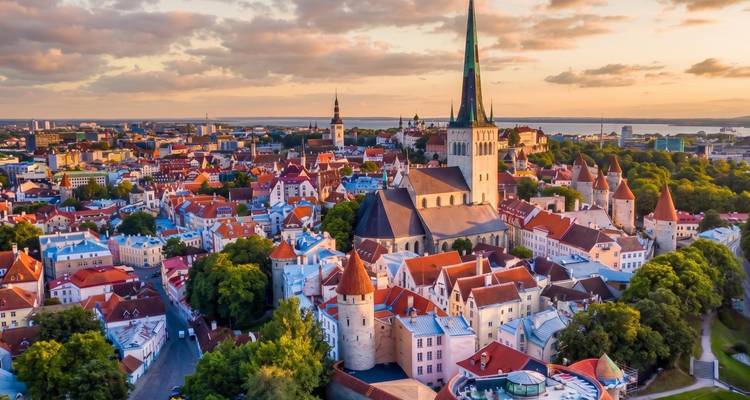 Luftaufnahme des Panoramas von Tallinns rotgedeckter Altstadt mit hohen Kirchenspitzen und umgebendem Meer bei Sonnenuntergang.