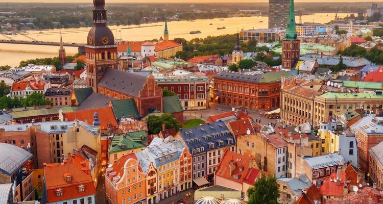 Luftaufnahme zur goldenen Stunde über Riga mit Daugava-Fluss, Kathedralenturm und bunten Dächern.
