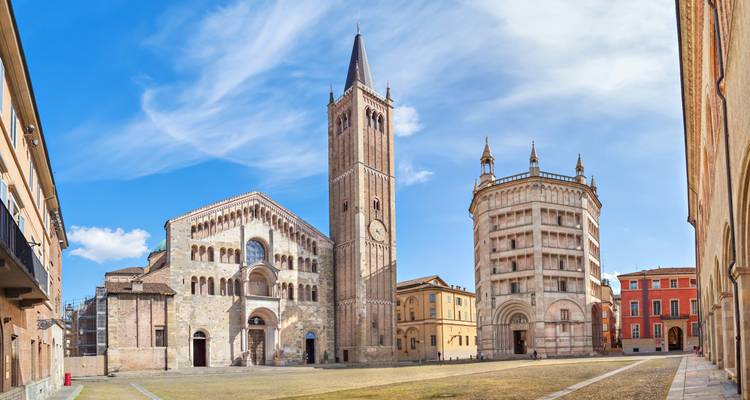 Panoramic view of Parma Cathedral, tall bell tower and octagonal Baptistery set against a clear blue sky.
