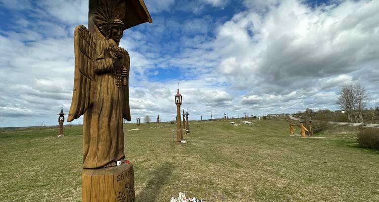 Vista amplia de una colina cubierta de pasto salpicada de estatuas de ángeles de madera tallada bajo un cielo parcialmente nublado.
