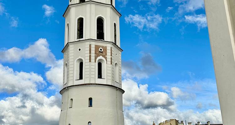 Torre de campanas blanca y alta de la Catedral de Vilna recortada contra un cielo azul brillante con nubes esponjosas.