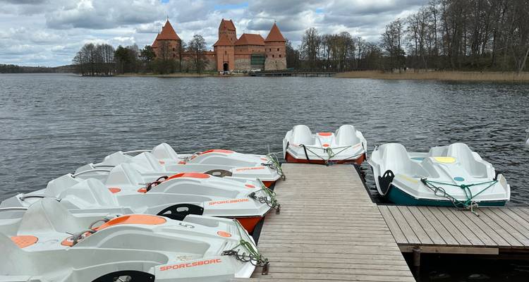 Fila de botes a pedal amarrados a un muelle de madera frente al Castillo de la Isla de Trakai al otro lado del lago.