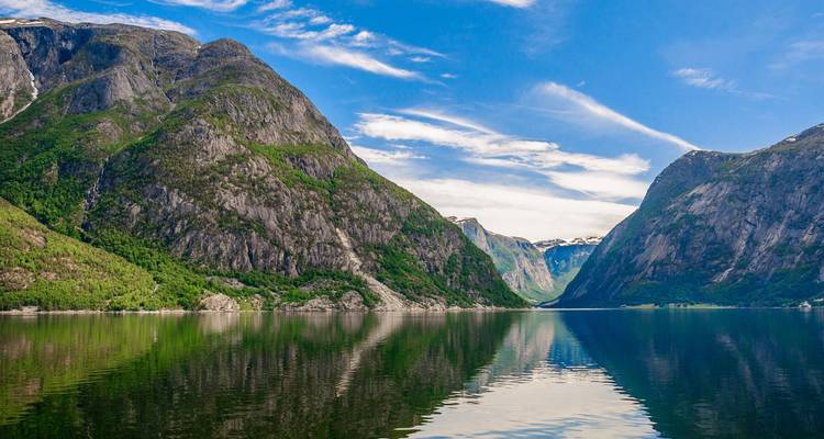 Un fjord norvégien tranquille encadré par des falaises imposantes se reflétant parfaitement dans une eau calme sous un ciel bleu.