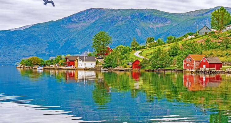 Les chaumières et les petites maisons flottantes aux couleurs vives se reflètent dans un fjord brillant, dominé par des montagnes verdoyantes.