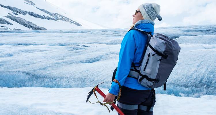 Une femme équipée d'un sac à dos et d'une piolet observe un champ de glacier sous la lumière du jour éclatante.