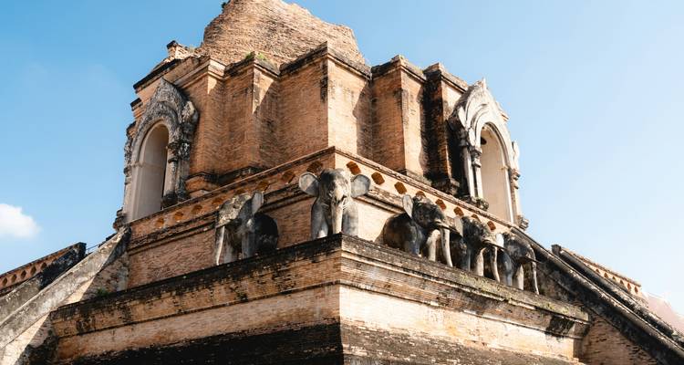 Base ornée d'éléphants du chédi de Wat Chedi Luang capturée à la lumière chaude du soleil et sous un ciel bleu.
