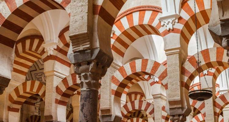 Les arches et les colonnes rayées emblématiques de la Mezquita de Cordoue, illuminées par une lumière intérieure douce.