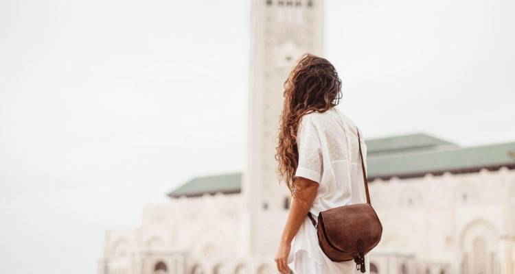 Vue arrière d'une femme vêtue de vêtements blancs amples admirant le minaret imposant d'une mosquée ornementée