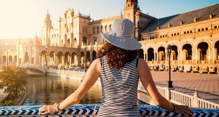 Vue arrière d'une femme vêtue d'une robe rayée et d'un chapeau admirant l'architecture ornée de la Plaza de España.