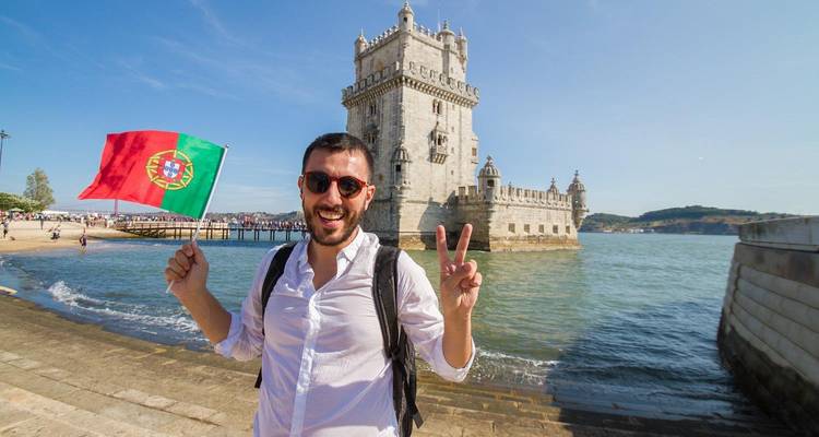 Voyageur souriant avec le drapeau portugais posant près de la Tour de Belém sur le Tage.