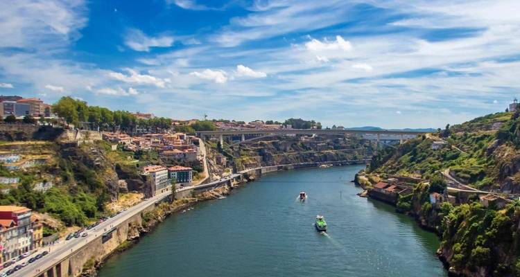 Vista expansiva del río Douro con un puente y barcos navegando entre colinas verdes.