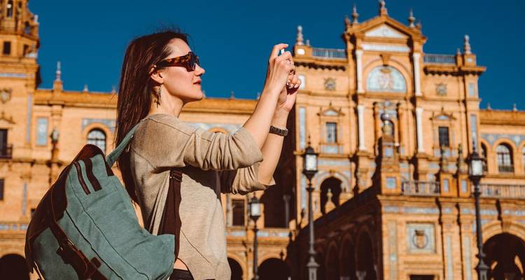 Una viajera fotografía la arquitectura de ladrillo ornamentada de la Plaza de España bajo la luz solar intensa.