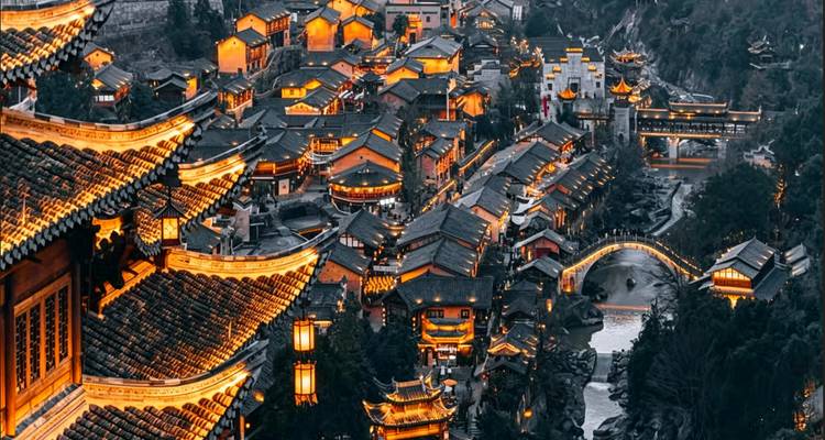 Una vista aérea espectacular de un pueblo ribereño de estilo antiguo, con tejados brillando en luces ámbar junto a un puente sinuoso.