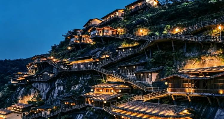 Pueblo en ladera iluminado por la cálida luz de faroles bajo un profundo cielo azul nocturno.