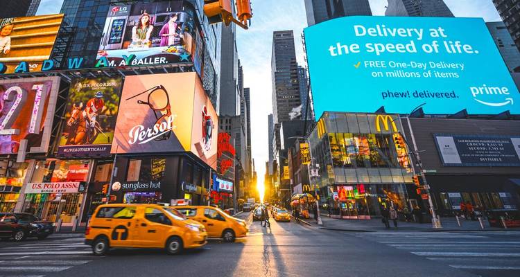Lebendige Times-Square-Szenerie mit gelben Taxis, aufragenden Werbetafeln und Fußgängern, während goldenes Sonnenlicht die Avenue hinabströmt