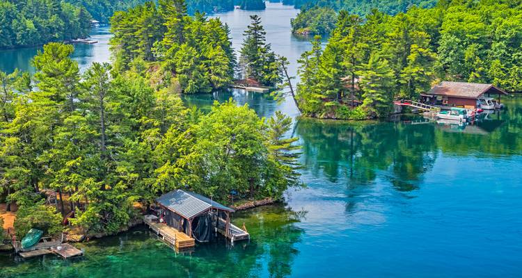 Serenissime See mit kleinen bewaldeten Inseln und Hütten in der Region der Tausend Inseln, die sich in klarem blauem Wasser spiegeln