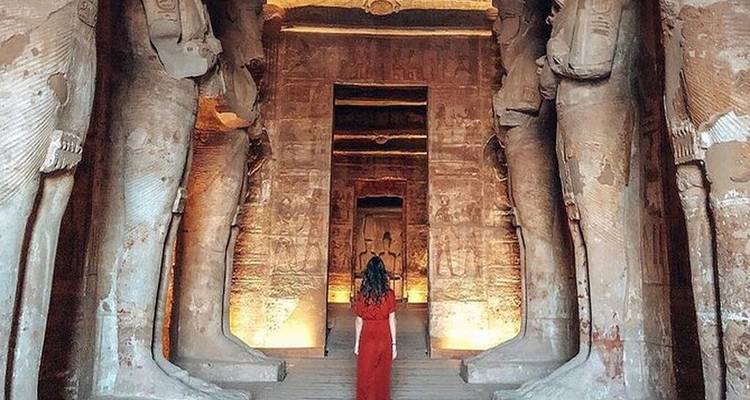 Eine Frau in einem roten Kleid geht durch eine großartige antike Tempelanlage mit imposanten Statuen.