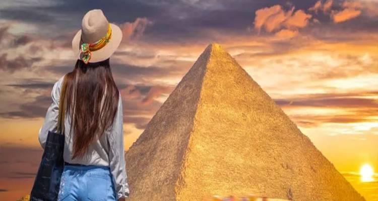 Junge Frau mit langen Haaren, die die Große Pyramide vor einem dramatischen Sonnenuntergangshimmel bewundert.