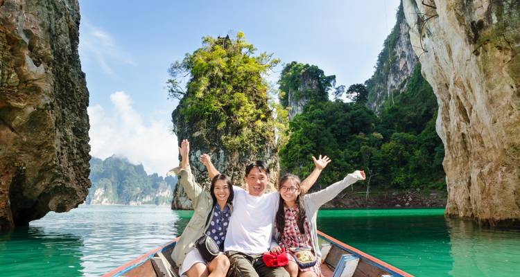 Familia sonriente posando en una barca de cola larga entre acantilados de piedra caliza imponentes y aguas de laguna color esmeralda.
