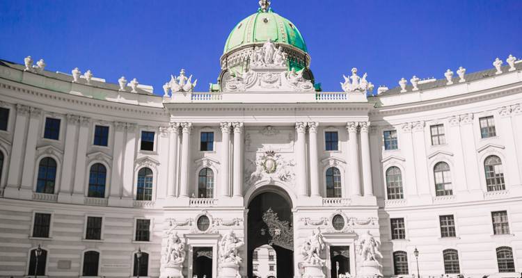 Façade baroque blanche de la Porte Michaeler du Palais de la Hofburg couronnée d'un dôme vert sous un ciel éclatant