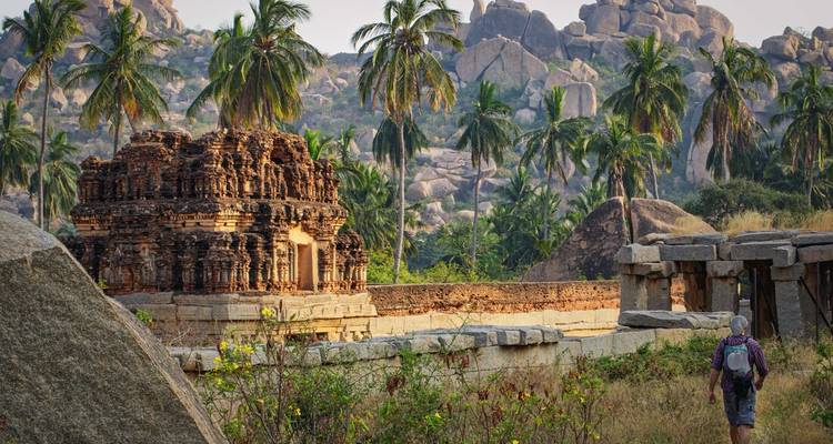 Temple en pierre ancienne et rochers parsemés de palmiers à Hampi avec un routard solitaire en exploration.