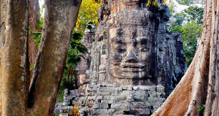 Torre de cara de piedra del templo Bayon enmarcada por árboles exuberantes en Angkor Thom, Camboya.