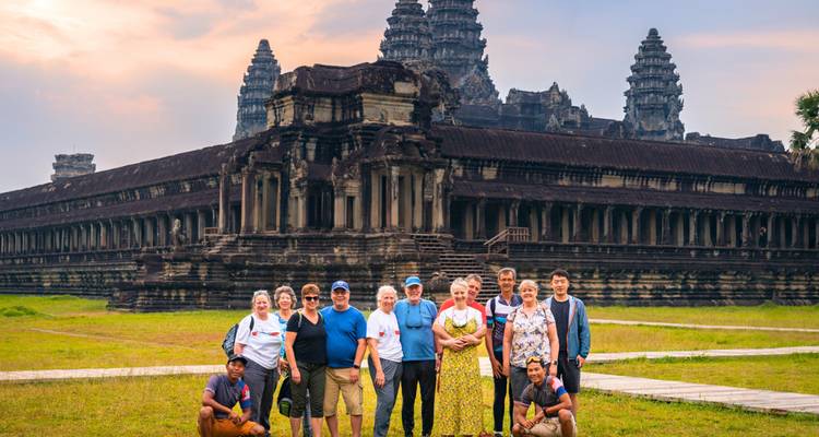 Grupo de turismo posando felizmente frente al icónico complejo del templo de Angkor Wat al atardecer.