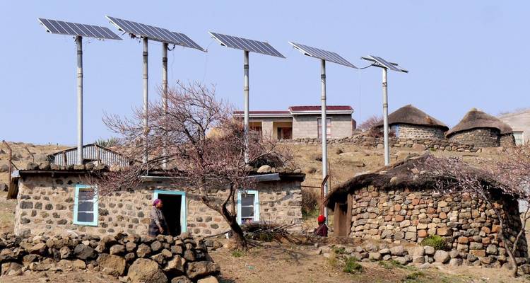Des maisons de village en pierre et chaume surmontées de panneaux solaires modernes au milieu d'un terrain rocheux et aride.