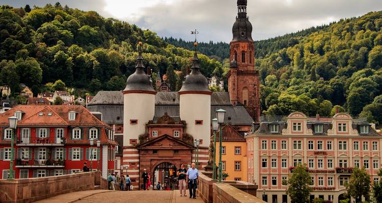 Puerta de la histórica puerta de piedra y coloridos edificios de la ciudad antigua de Heidelberg con colinas boscosas detrás.