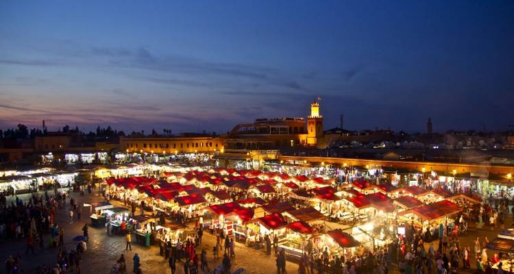 Panorama en soirée de la place Jemaa el-Fnaa animée par des étals de nourriture illuminés et des foules à l'heure bleue