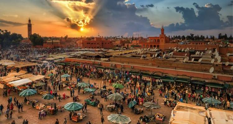 Les rayons du coucher de soleil percent les nuages au-dessus du marché animé de Marrakech, rempli de vendeurs et de visiteurs
